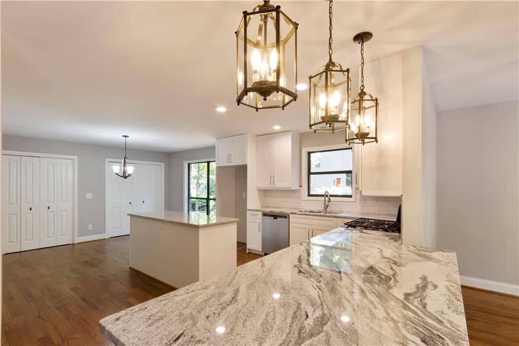 Kitchen remodel with marble-look counters, white cabinetry, brass lantern pendants, and an oversized island.
