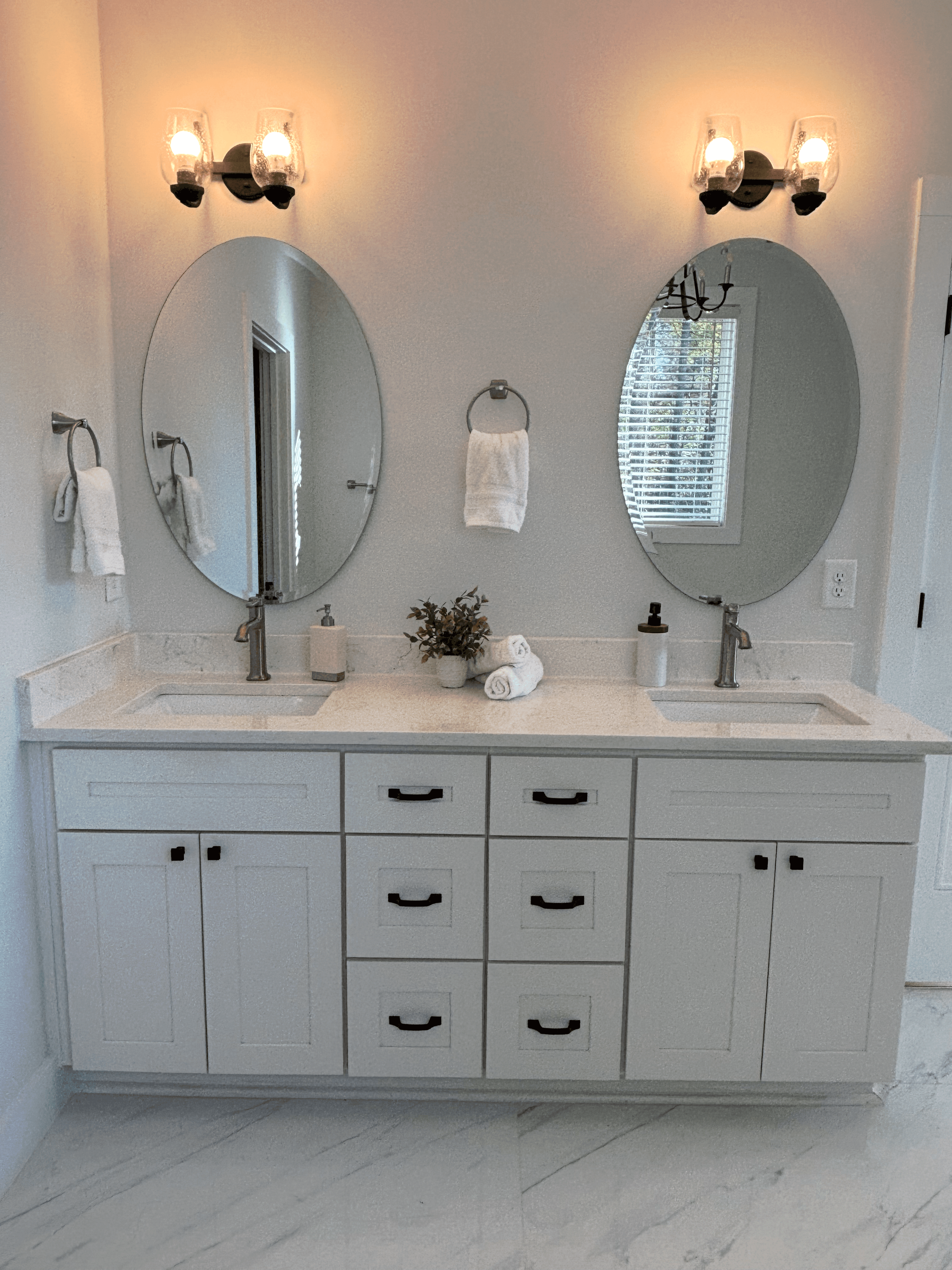 Bathroom double vanity with white cabinetry, oval mirrors, black hardware, and marble-look surfaces.