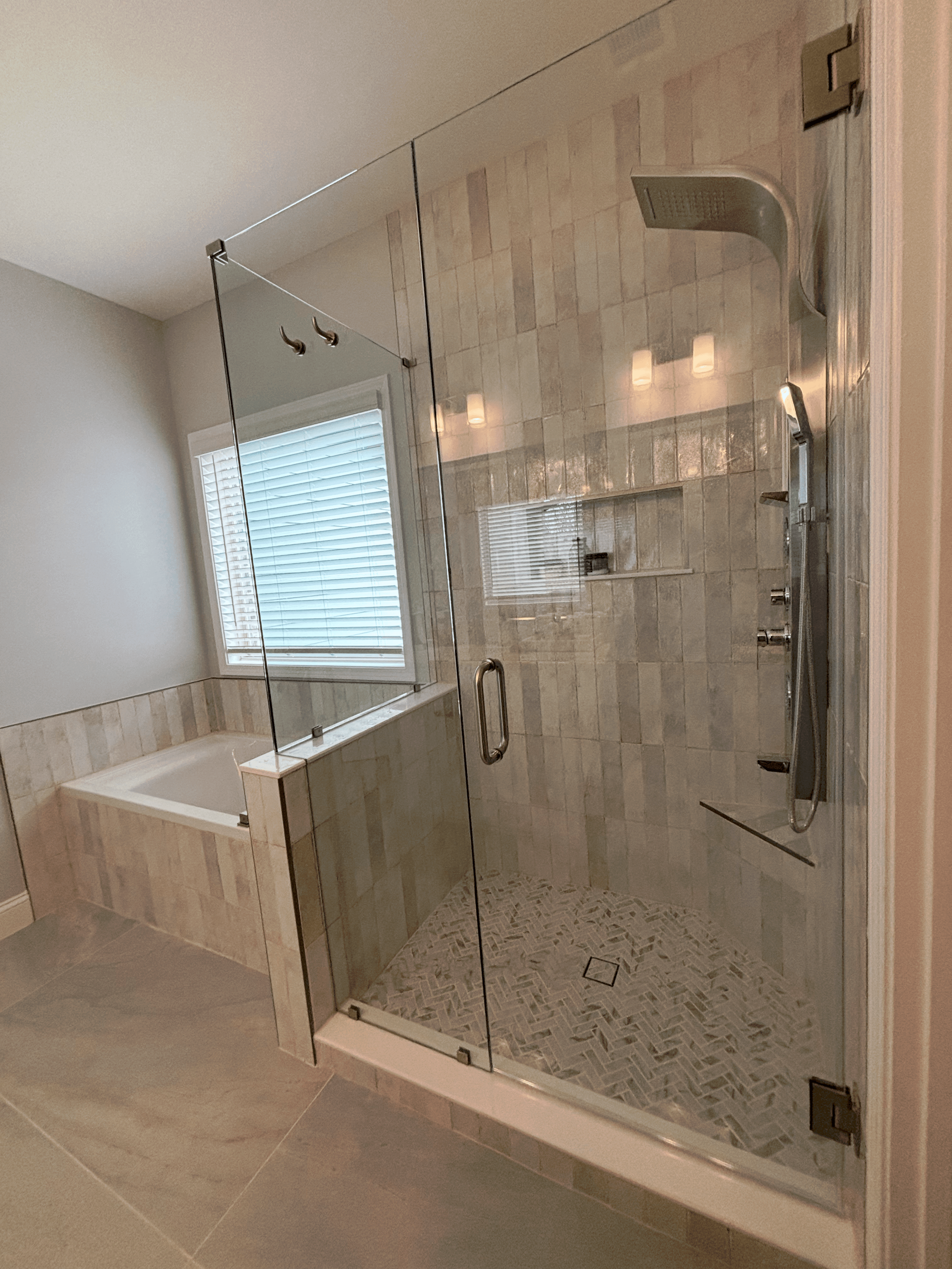 Primary bathroom with a frameless glass shower, soaking tub, and light tile finishes.