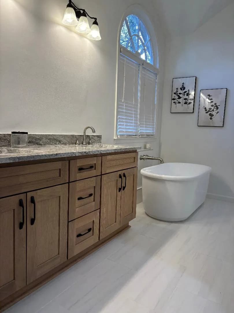 Bathroom with a soaking tub beneath an arched window and a soft, bright palette.