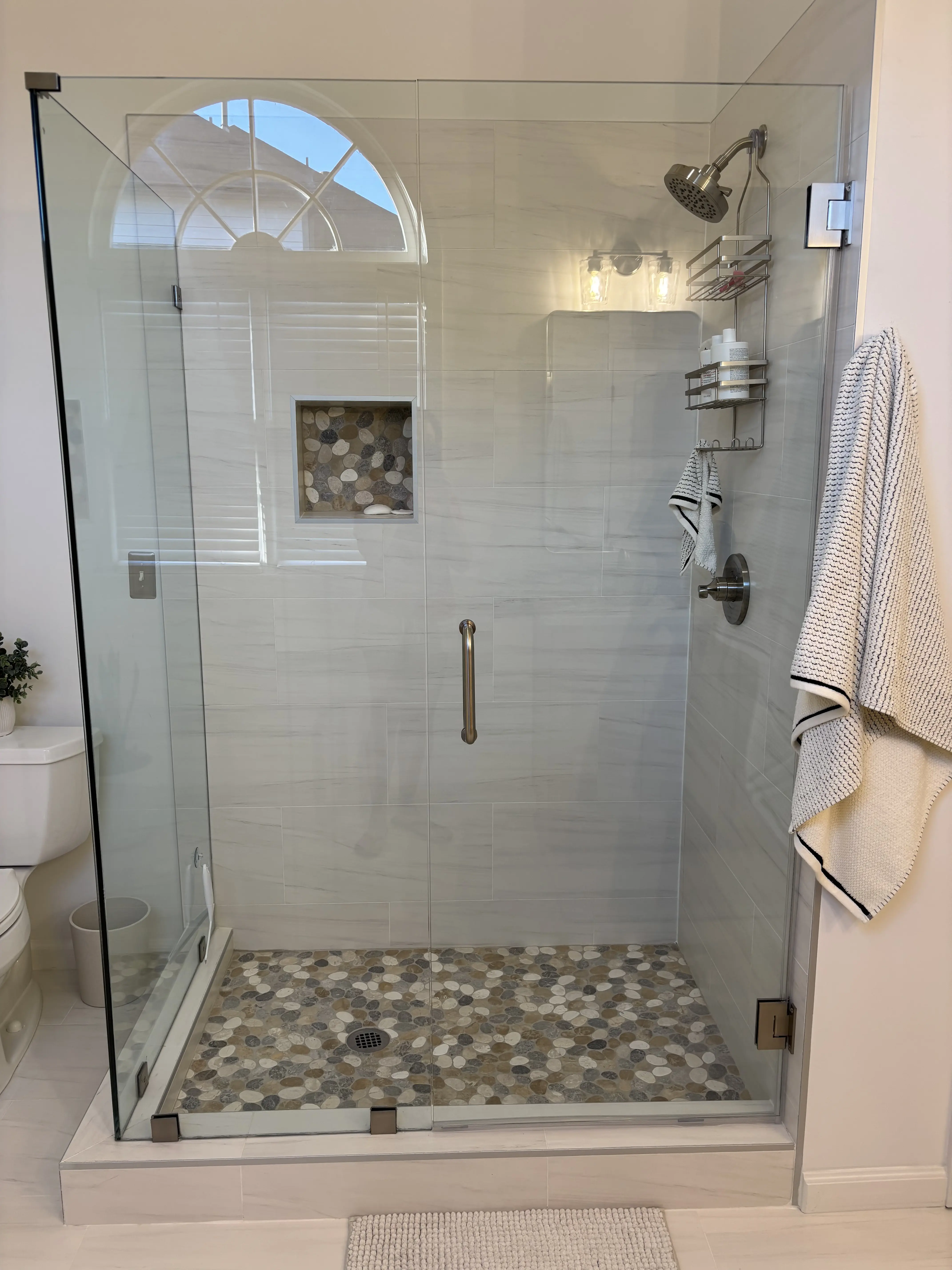 Front view of a frameless glass shower with bright tile and polished fixtures.