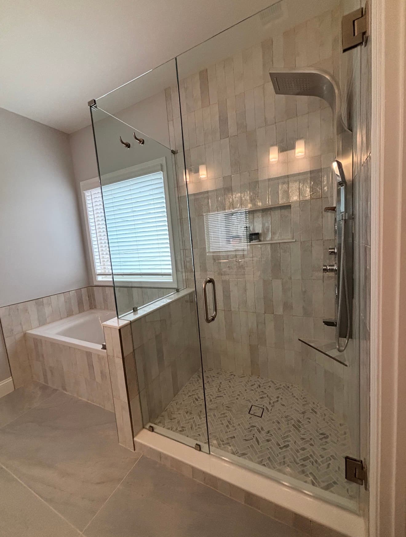 Bathroom remodel with a freestanding tub beside a glass shower, pale tile walls, and a bright window.