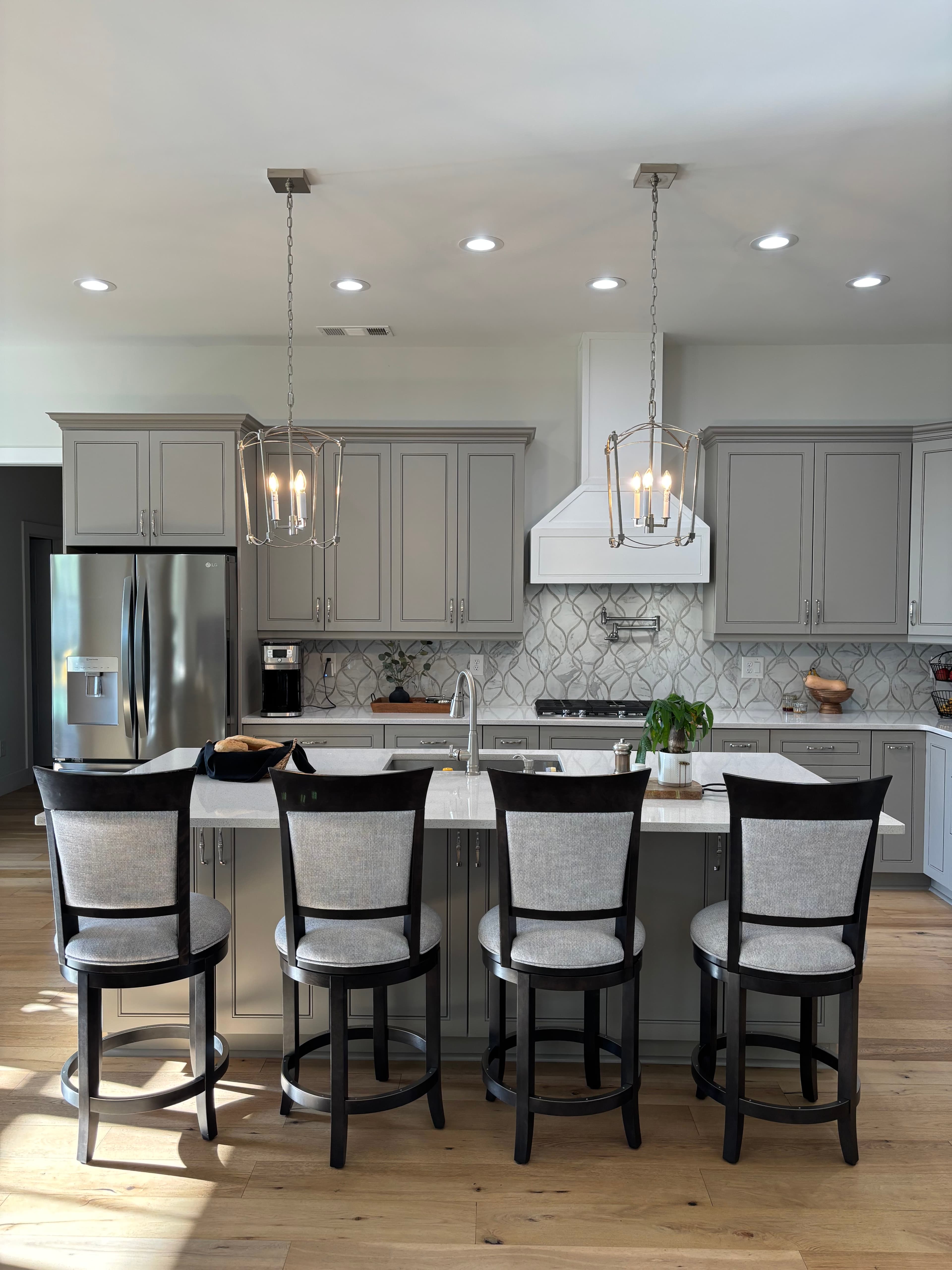 Kitchen renovation with gray shaker cabinetry, island seating, pendant lighting, and warm wood floors.