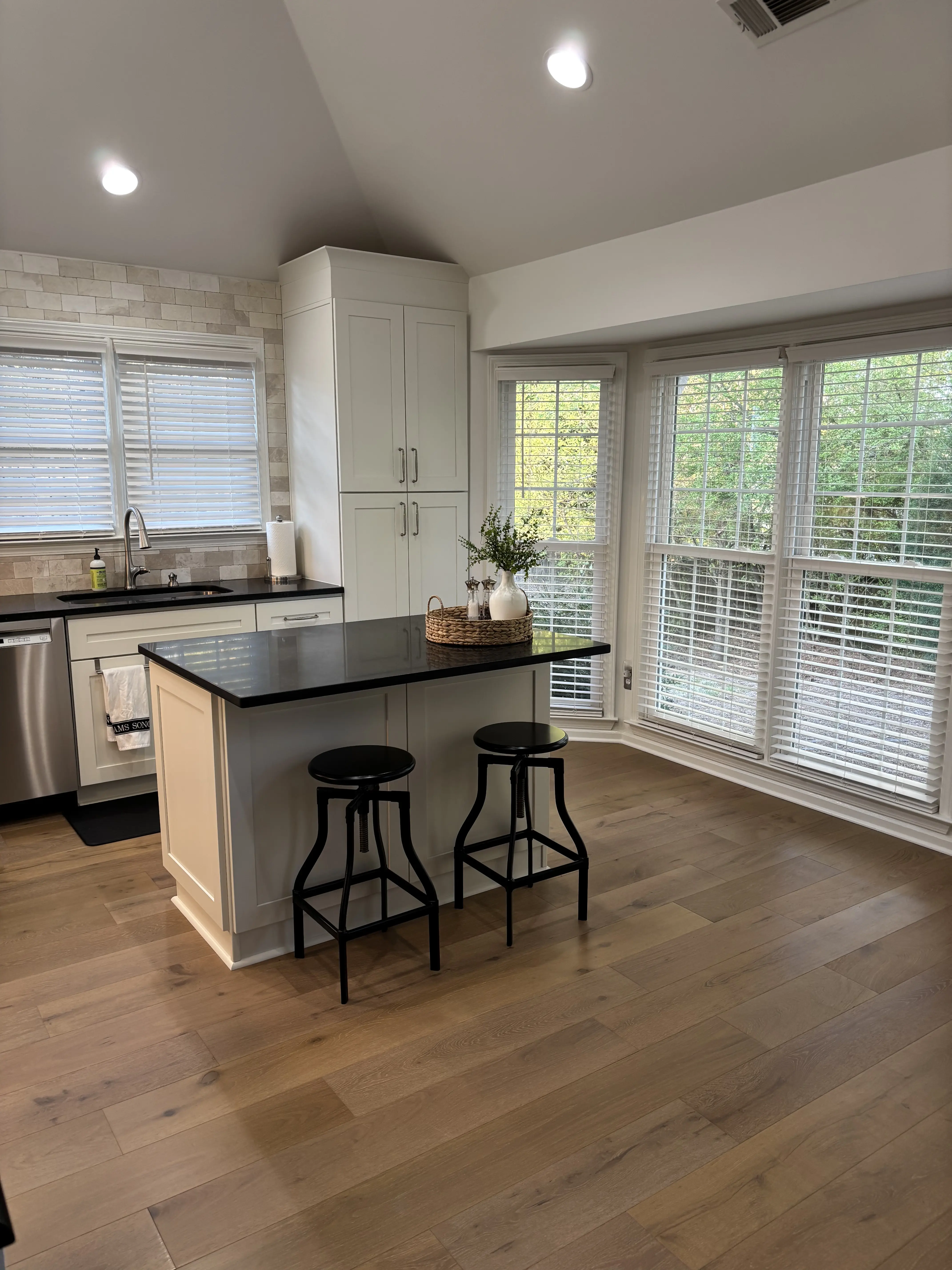 Kitchen renovation with a black-topped island, light shaker cabinetry, and a bright wall of windows.