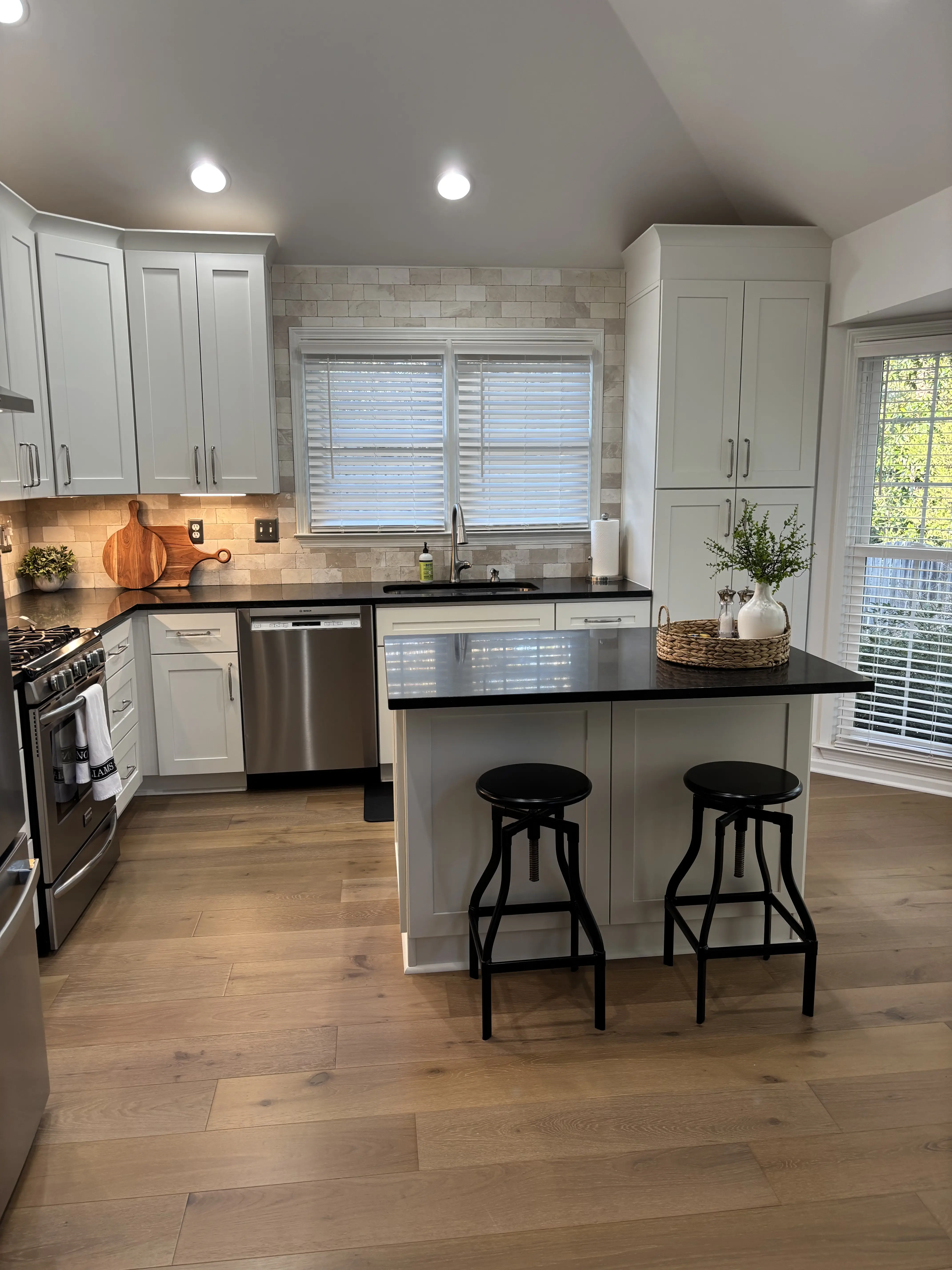 Kitchen renovation with a black island, light shaker cabinets, and warm wood flooring.